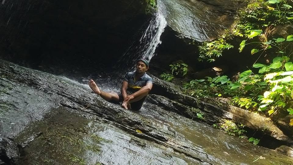Sitting on wet rock beneath a waterfall running down a dark rock face